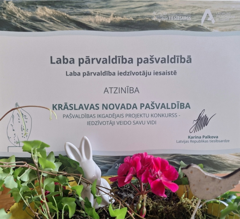 Tiesībsarga atzinības diploms uz galda kopā ar augiem un dzīvnieku figūriņām