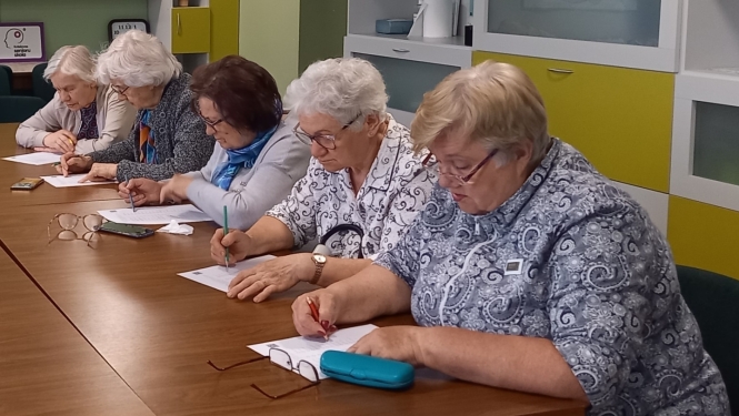 Seniori sēž pie galda un pilda rakstisku uzdevumu