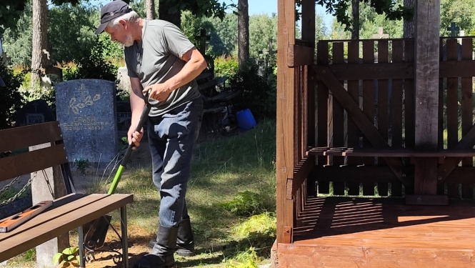 Cilvēks labiekārto koka kapličas apkārtni