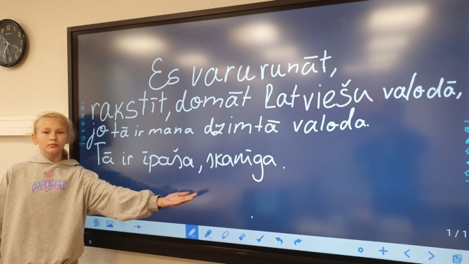 Skolniece pie interaktīvās tāfeles prezentē latviešu valodas uzdevumu