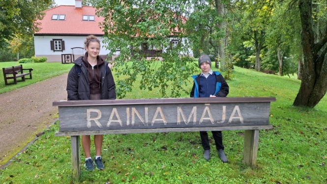 Divi skolēni pie „Raiņa mājas” zīmes