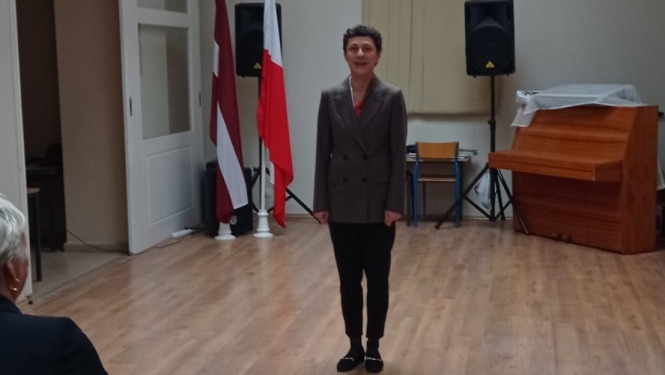 Cilvēks zālē pie Latvijas un Polijas karogiem
