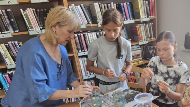 Bibliotekāre kopā ar divām meitenēm veido lukturīšus