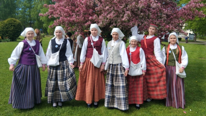 Meitenes tautastērpos pozē pie ziedoša koka parkā