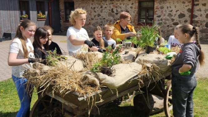 Bērni ar skolotāju piedalās dārza darbos