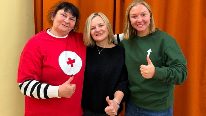 Trīs sievietes pozē fotogrāfijai pie oranža aizkara