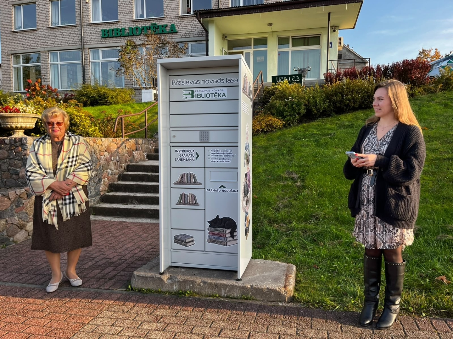Divas sievietes pie bibliotēkas grāmatu nodošanas skapja