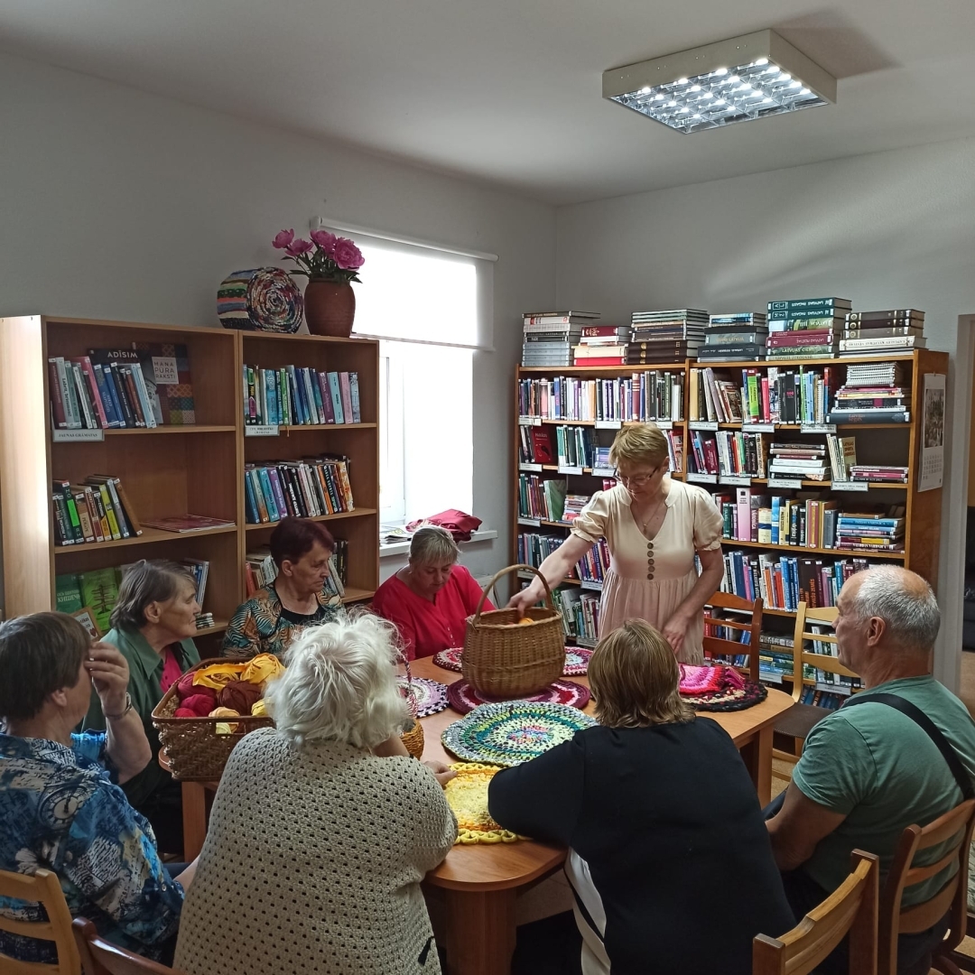 Cilvēku grupa bibliotēkā piedalās tamborēšanas paklāju meistarklasē