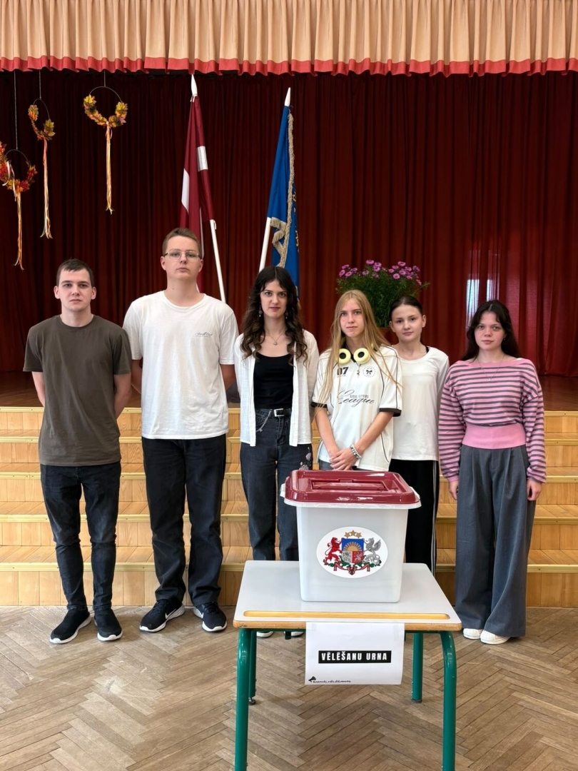 Seši jaunieši pie vēlēšanu urnas skolas zālē
