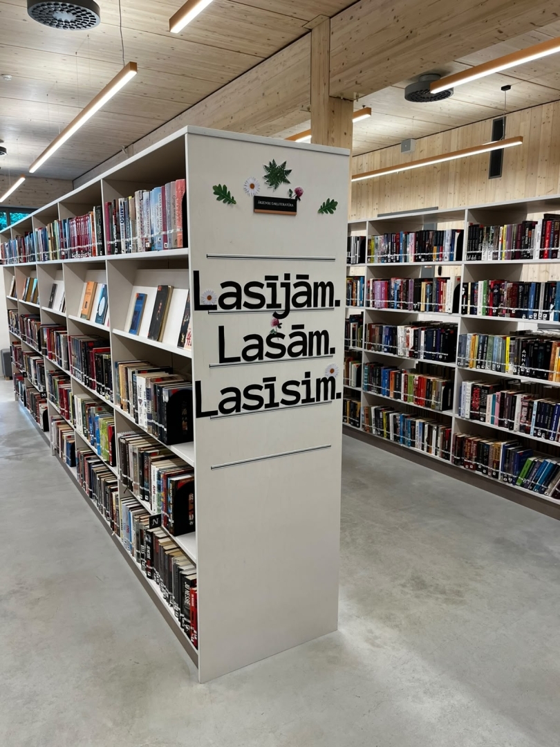 Plaša bibliotēkas grāmatu zona ar plauktiem un uzrakstu “Lasījām. Lasām. Lasīsim.”