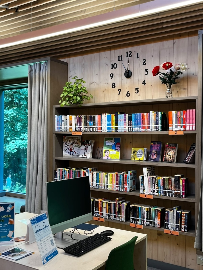Bibliotēkas darba vieta ar datoru un grāmatu plauktiem