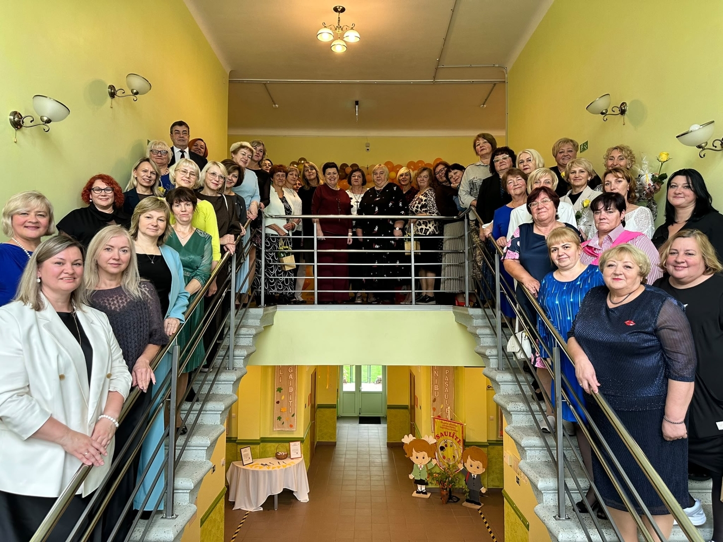 Liela cilvēku grupa pozē uz kāpnēm