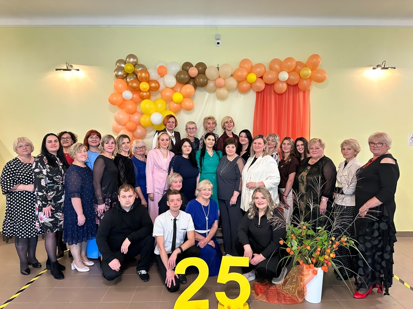 Cilvēki pozē pie svētku dekorācijām ar skaitli „25”