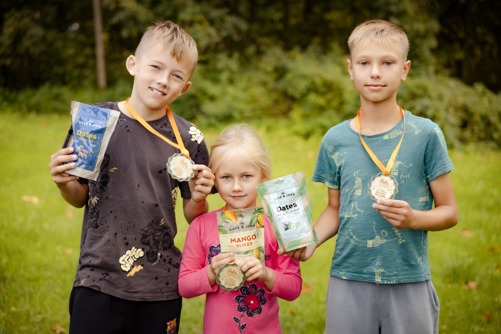 Trīs dalībnieki ar medaļām un našķiem