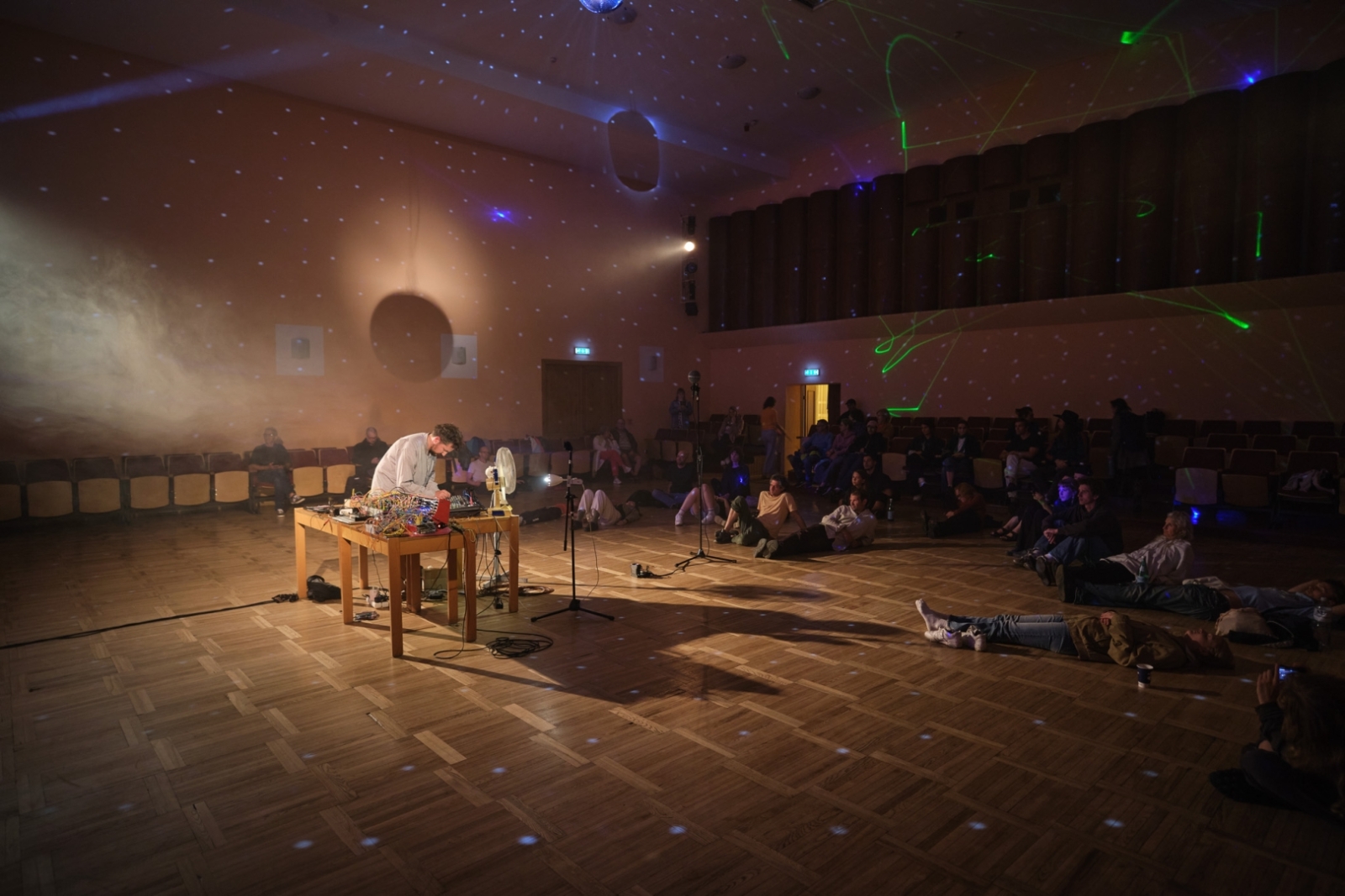 Elektroniskās mūzikas performance koncertzālē ar sēdošu un guļošu auditoriju