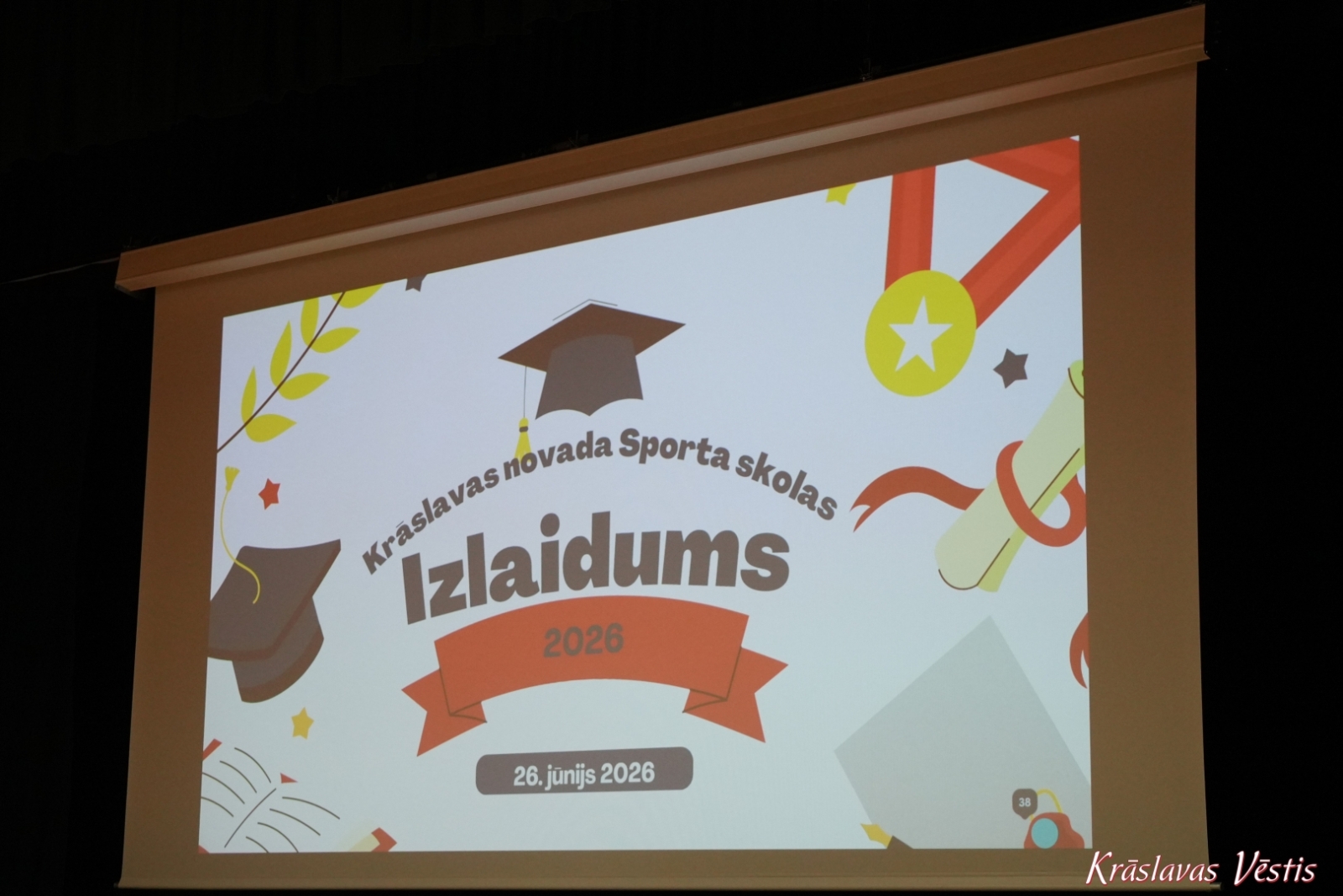 Uzraksts uz projektora ekrana “Krāslavas novada Sporta skolas Izlaidums 2026”