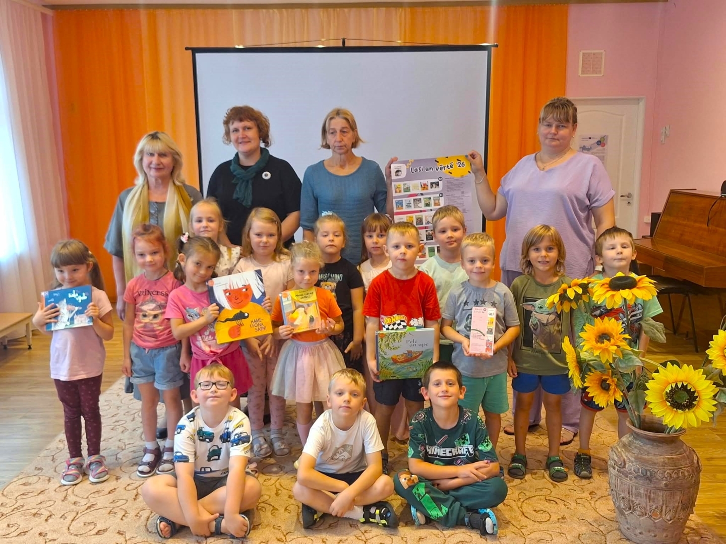 Bērnu grupa ar skolotājām un grāmatām
