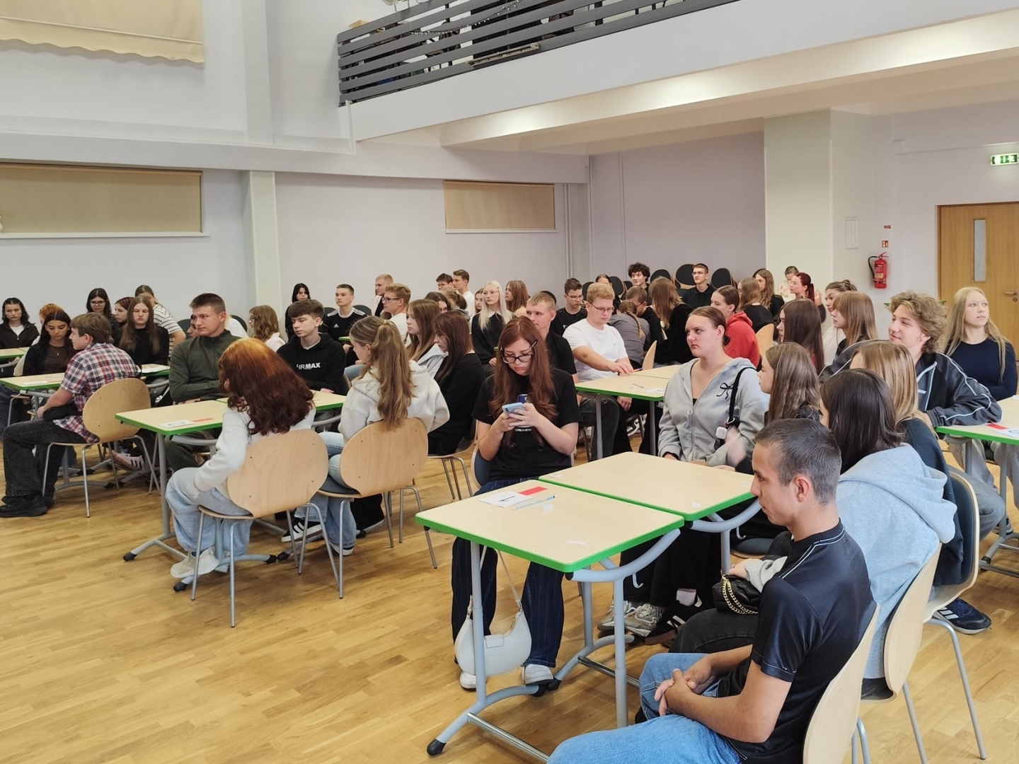Jaunieši sēž grupās pie galdiem un piedalās pasākuma aktivitātēs