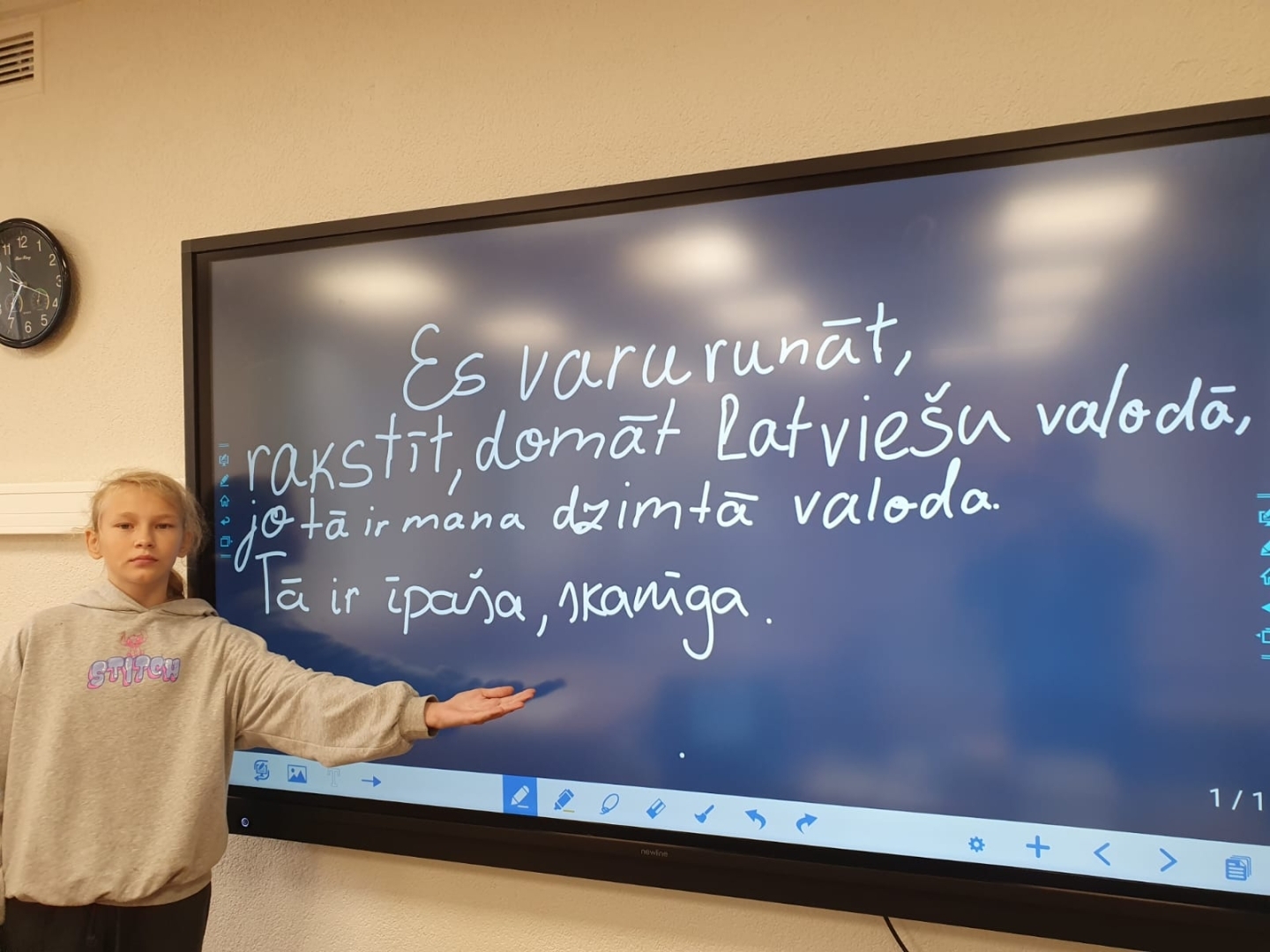 Skolniece pie interaktīvās tāfeles prezentē latviešu valodas uzdevumu