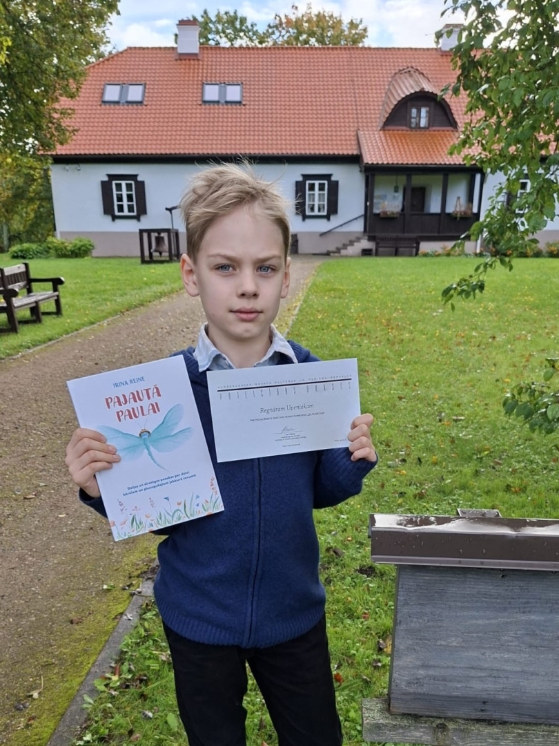 Skolēns ar grāmatu un atzinības rakstu pie Raiņa mājas