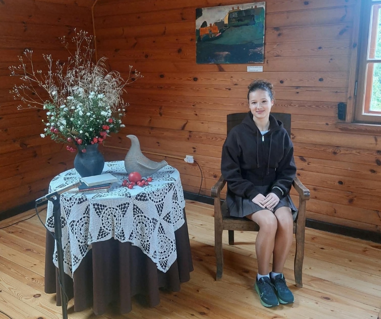 Skolniece sēž Raiņa mājas koka interjerā pie galda