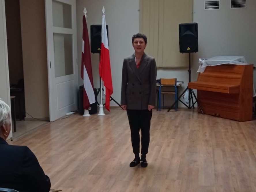 Cilvēks zālē pie Latvijas un Polijas karogiem