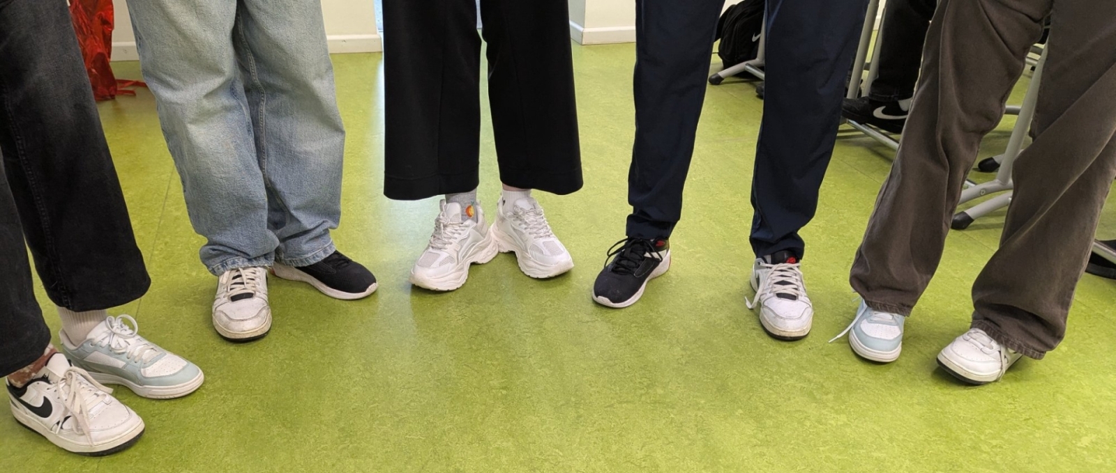 Skolēnu kājas un dažādi sporta apavi uz zaļas grīdas