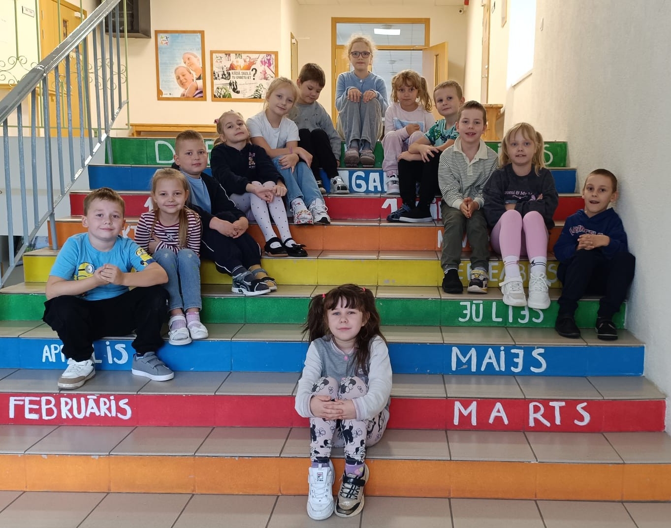 Bērnu grupa sēž uz krāsainām skolas kāpnēm