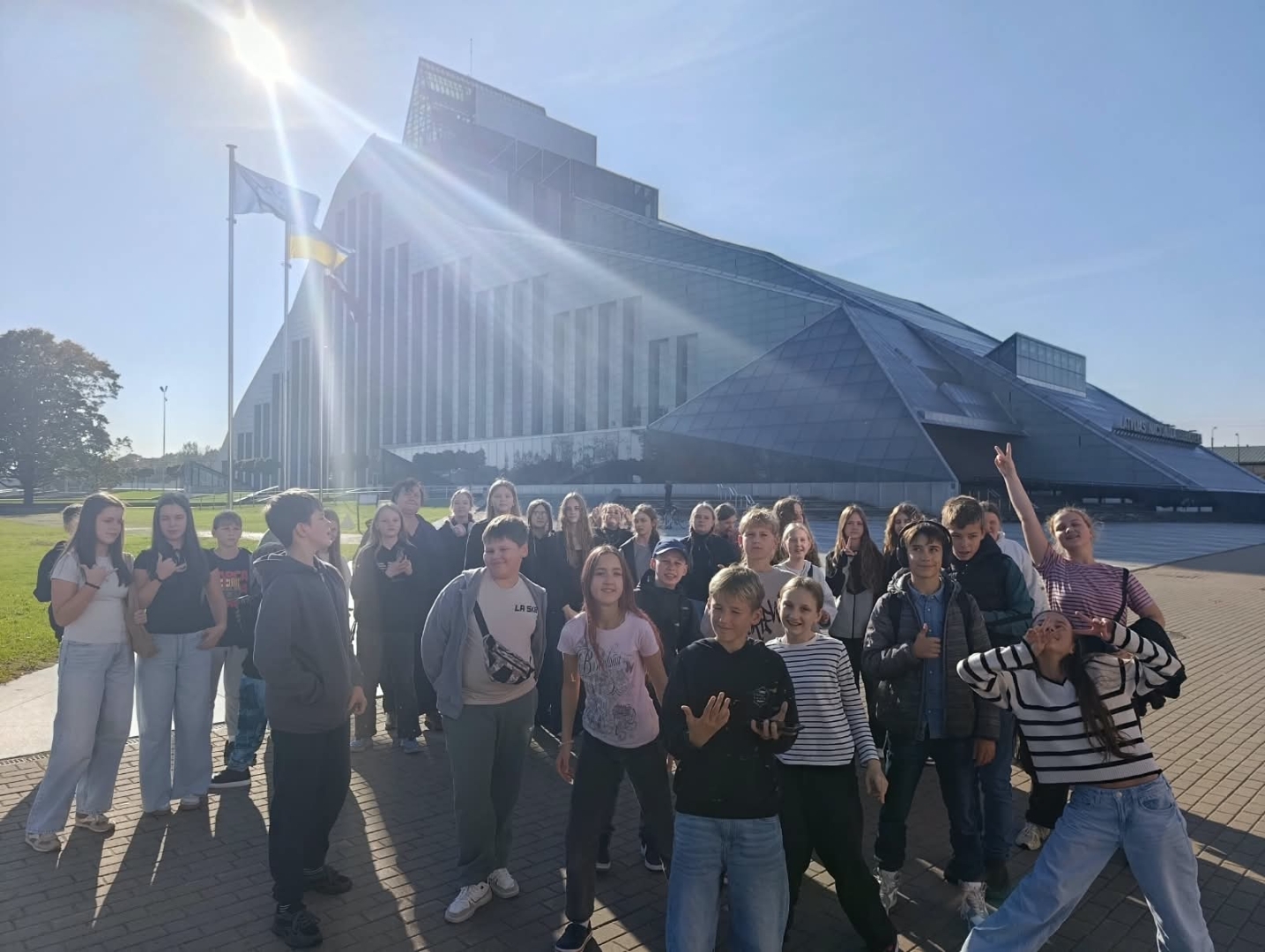 Skolēnu grupa pozē pie Latvijas Nacionālās bibliotēkas ēkas