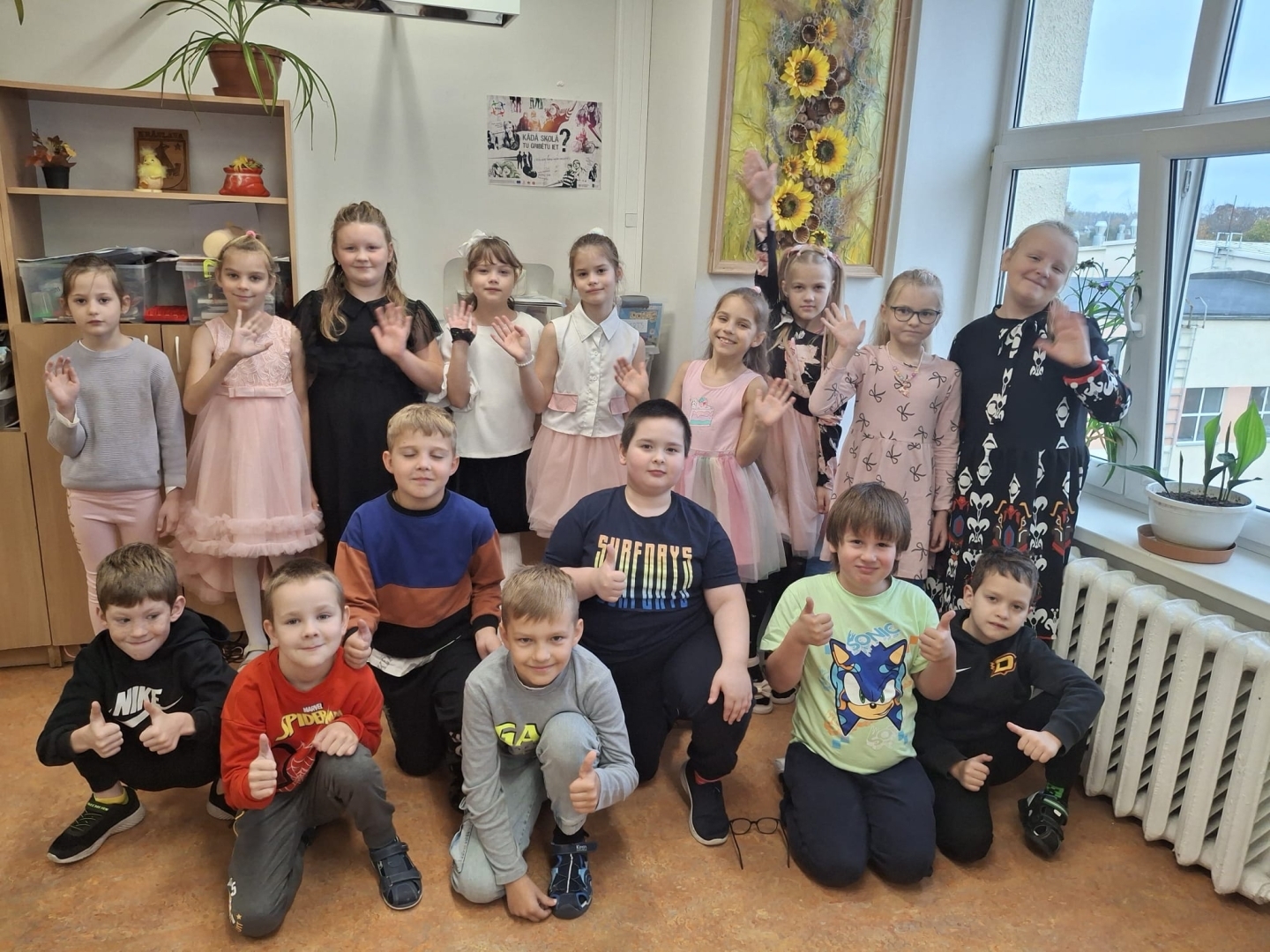 Skolēnu grupa kopā pozē un māj ar rokām