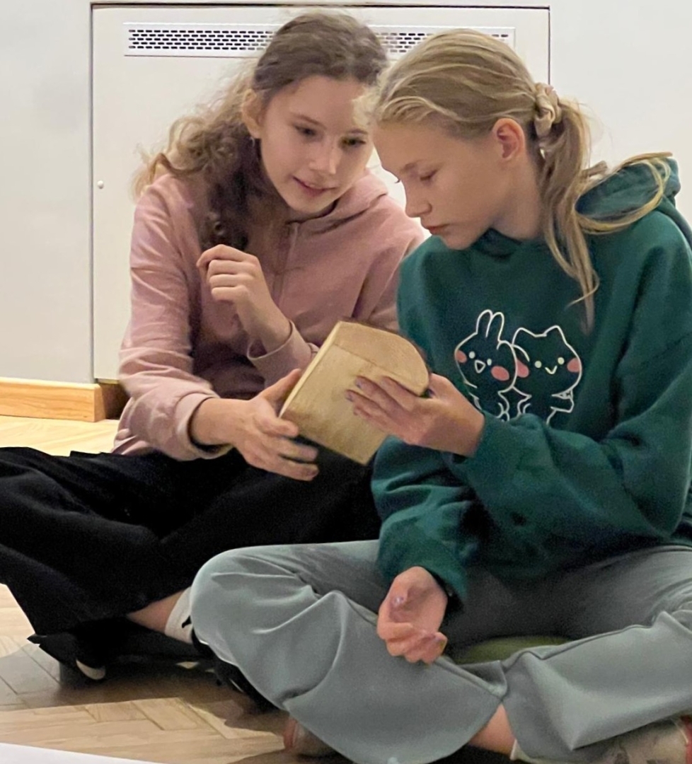 Divas skolnieces kopīgi pēta koka priekšmetu