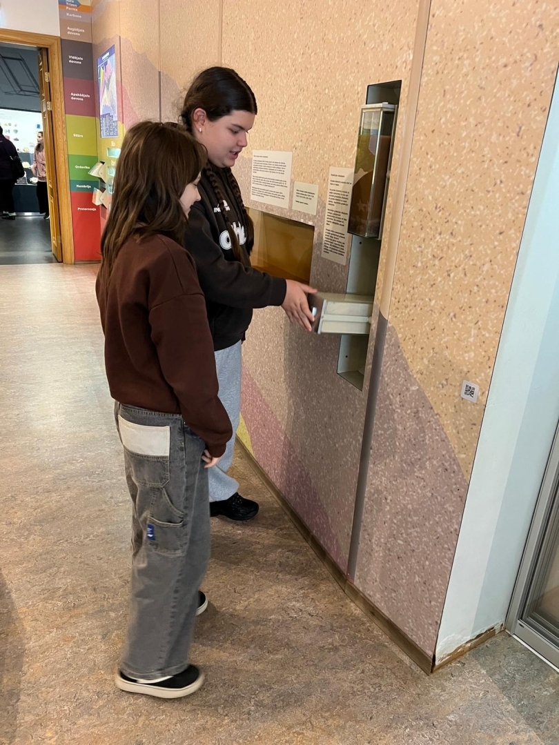 Divas skolnieces pēta interaktīvu muzeja eksponātu