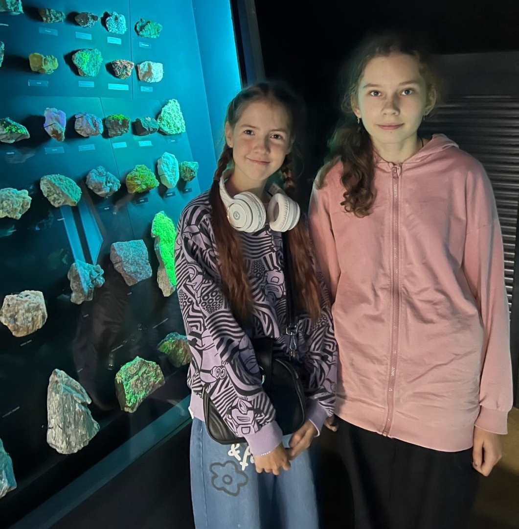 Divas skolnieces pēta minerālu kolekciju izgaismotā vitrīnā