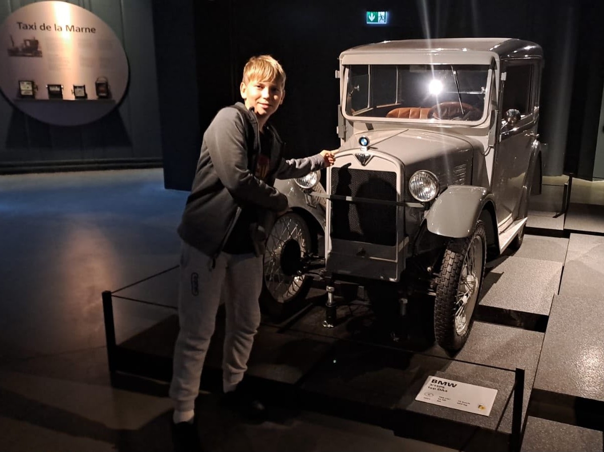 Skolēns pie vēsturiskas BMW automašīnas muzejā
