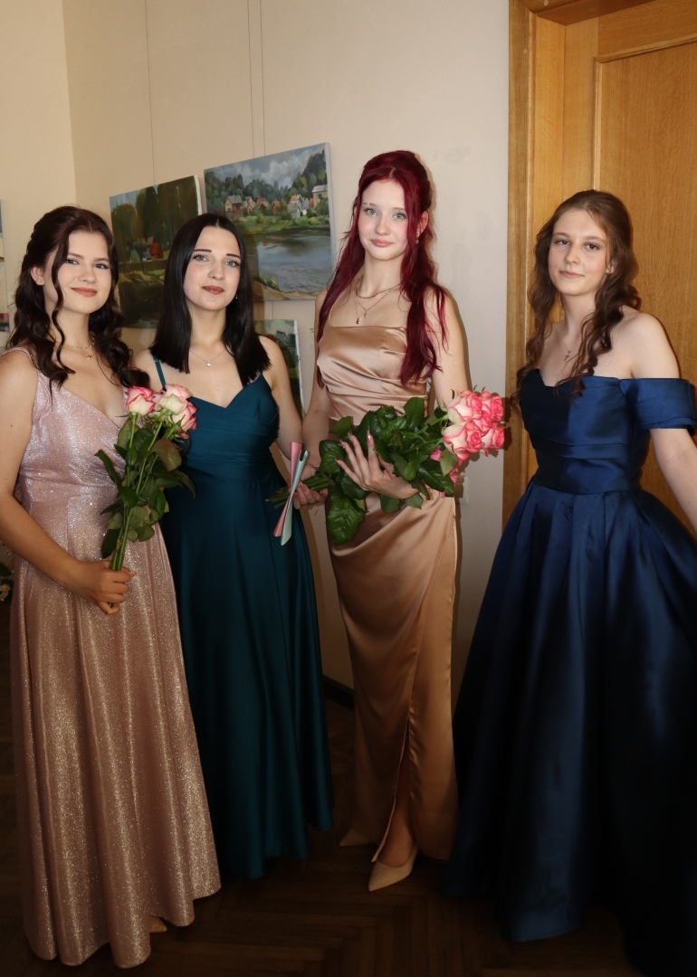 Četras absolventes ar rozēm pozē fotogrāfijai