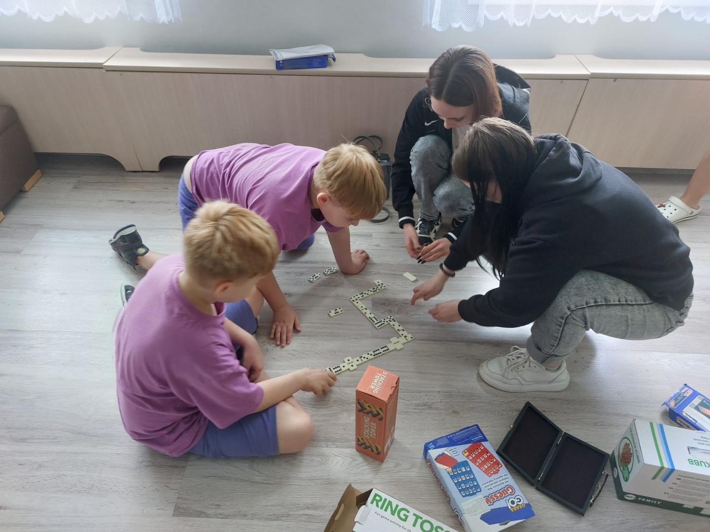 Bērni un jaunietes uz grīdas kopā spēlē domino