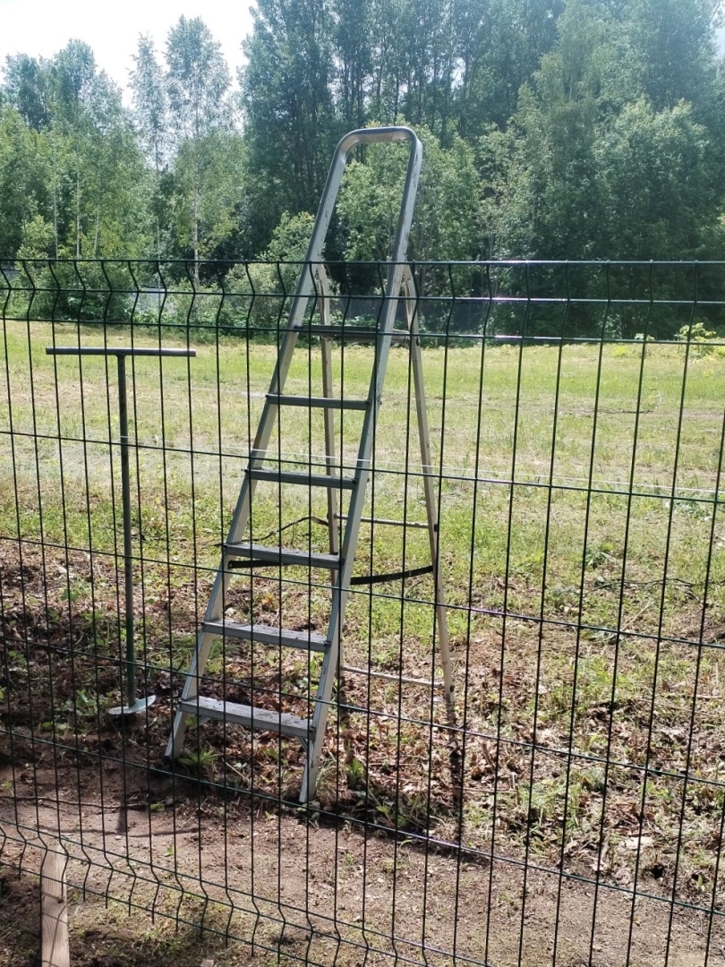 Metāla kāpnes pie zaļa žoga