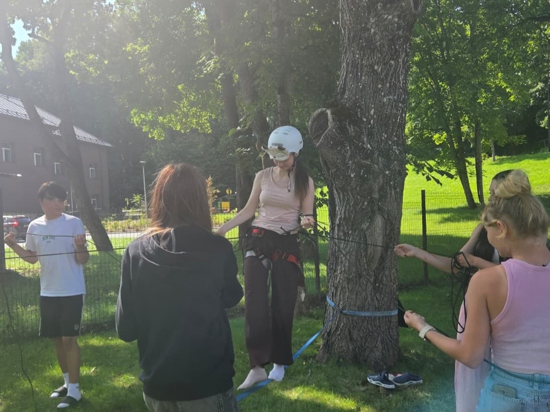 Dalībniece drošināšanas ekipējumā balansē uz troses