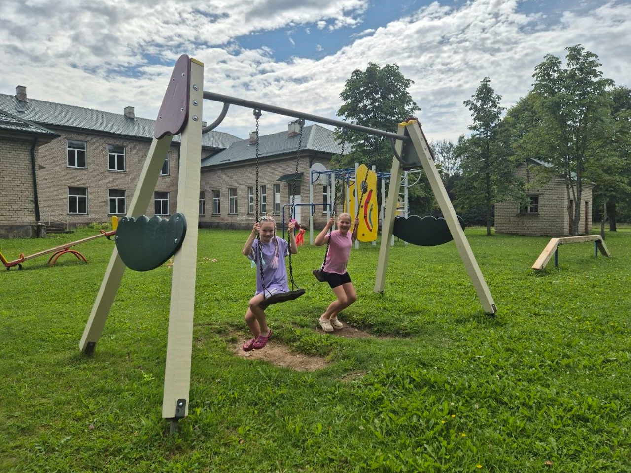 Bērni šūpojas rotaļu laukuma šūpolēs