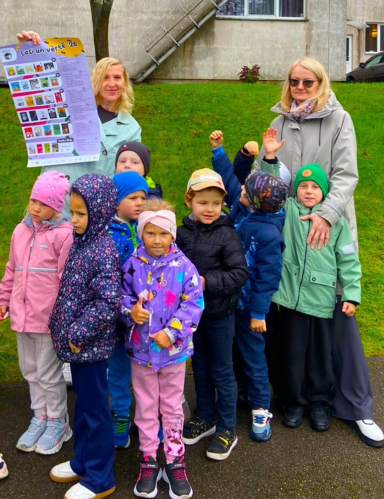 Bērni un pieaugušie ar lasīšanas akcijas plakātu