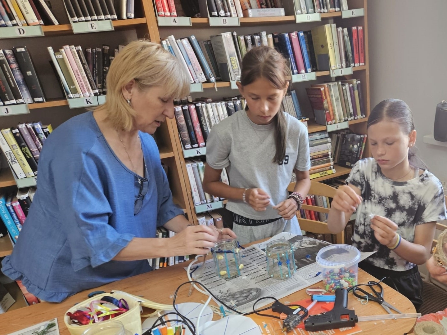 Bibliotekāre kopā ar divām meitenēm veido lukturīšus