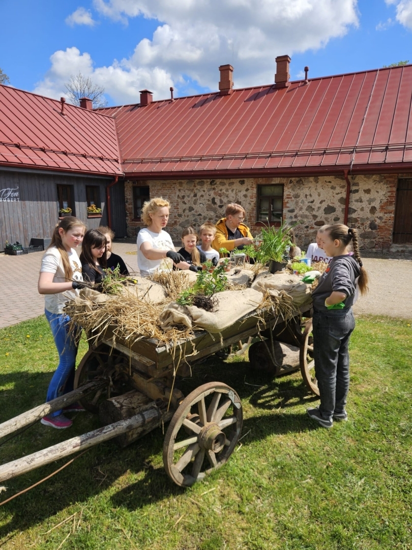 Bērni ar skolotāju piedalās dārza darbos