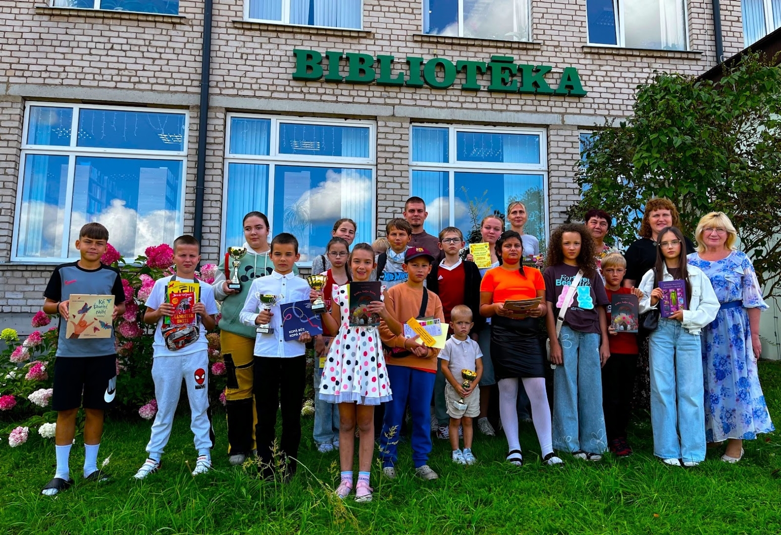 Bērni un pieaugušie pie bibliotēkas