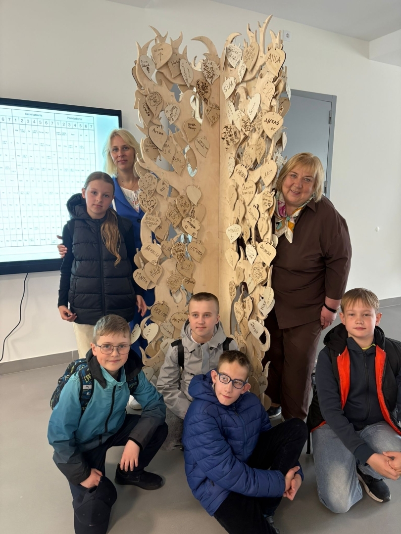 Skolēni un skolotājas pie draudzības koka ar gravētām sirsniņām