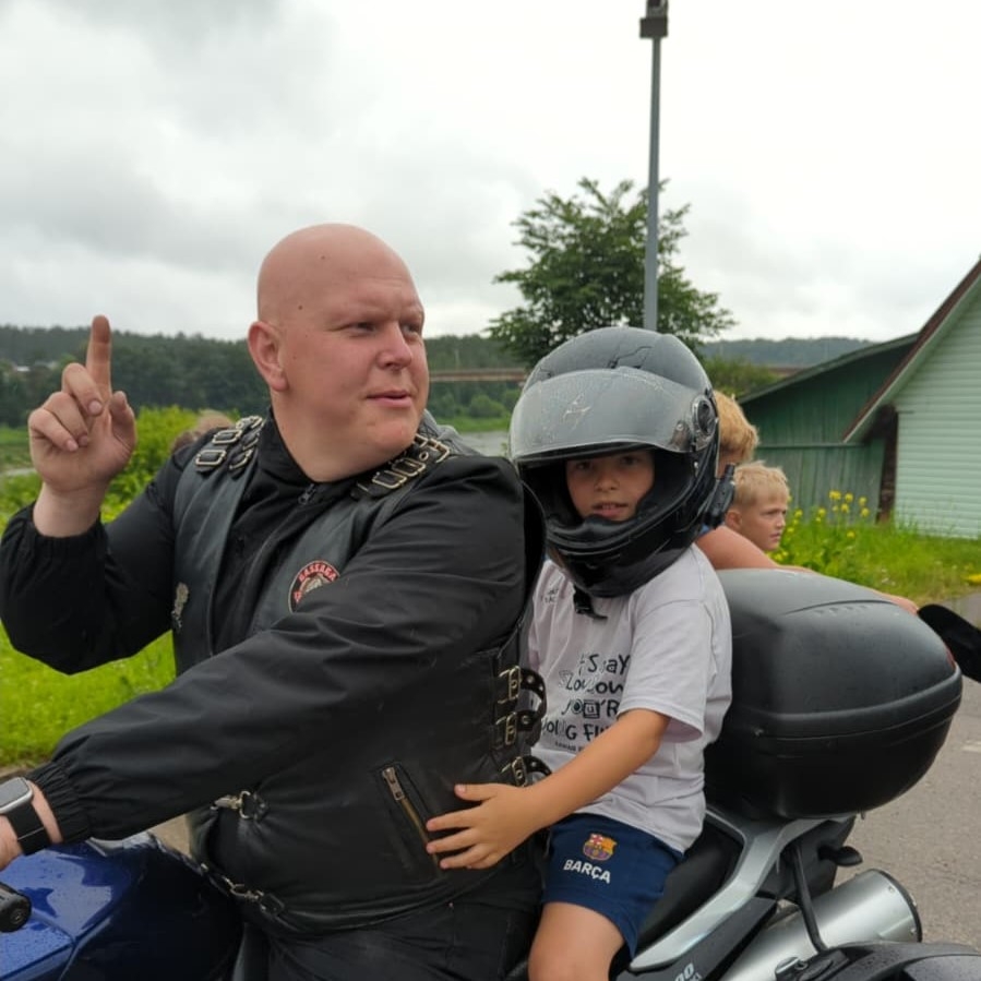 Bērns ķiverē sēž uz motocikla kopā ar motociklistu drošā demonstrējumā
