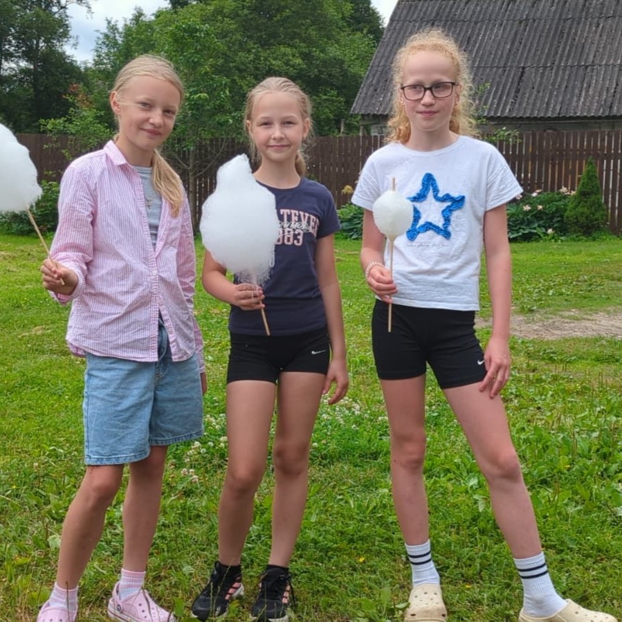 Trīs meitenes ārā tur rokās cukurvati un smaida
