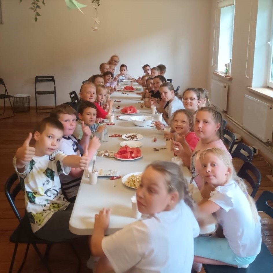 Bērni vasaras nometnē kopīgi bauda uzkodas pie gara galda