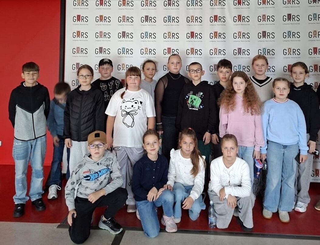 Bērnu grupa pie GORS logo sienas