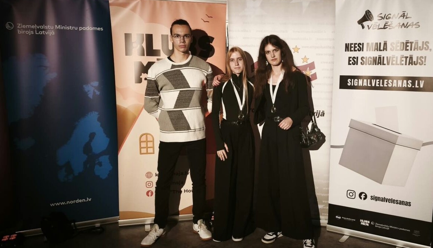 Jaunieši pozē pie informatīvajiem stendiem par projektu