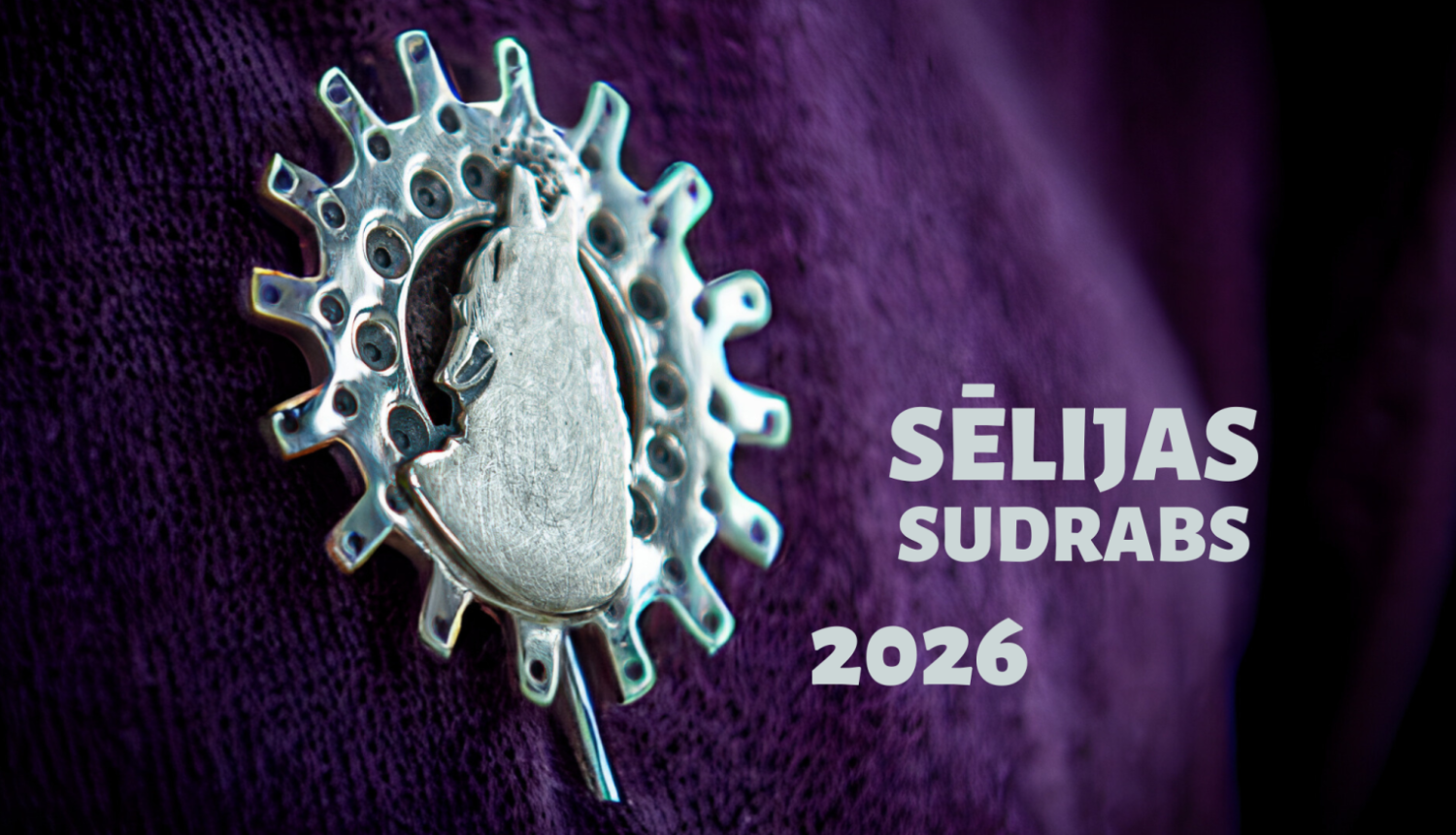 Sudraba rotaslieta uz tumši violeta auduma fona ar uzrakstu „Sēlijas sudrabs 2026”